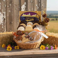 Load image into Gallery viewer, Gift basket with cookies and a decorative box on a wooden surface with flowers and hay bales in the background.
