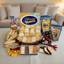 Load image into Gallery viewer, Assorted cookies, fudge, nuts, popcorn, acaroons, biscotti, chocolates and treats displayed on a table with a blurred Christmas tree in the background
